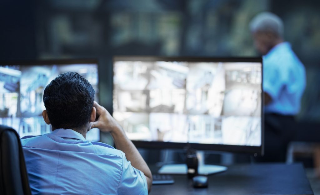 Security guard in control room, man checking cctv screen in surveillance office for building safety